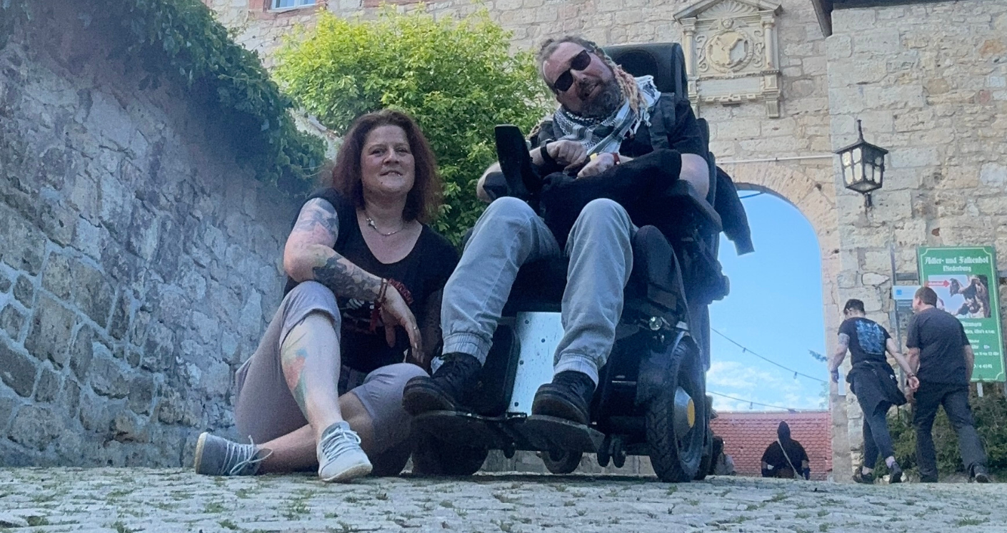 Eine Dame sitzt neben einem Mann im Rollstuhl